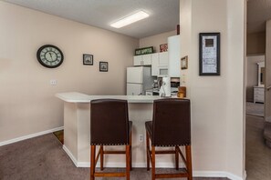 A compact kitchen with a white countertop, two wooden bar stools, a clock, and framed pictures on the wall. - Last Minute Disney Getaway! Townhouse with Private Pool. Book Now! #109037 (Orlando)