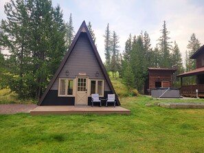 Una cabaña de forma triangular con terraza, dos sillas y una pequeña zona de piscina.