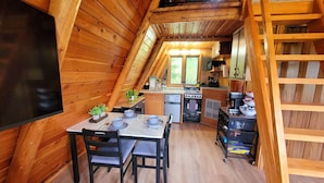 Un intérieur en bois comprenant une table à manger, des chaises, un coin cuisine et un espace en mezzanine.