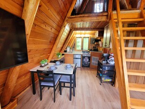 Un interior de madera con una mesa de comedor, sillas, una zona de cocina y un espacio en loft.