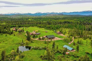 Una propiedad rural con varias cabañas, un estanque y una zona boscosa con montañas al fondo.