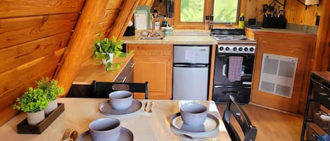 Una cocina acogedora con paredes de madera, una mesa de comedor preparada para dos personas y vistas al exterior a través de una ventana.