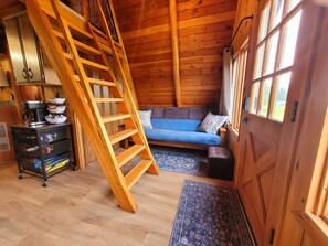 Interior de madera con una cama en literas, un sofá, una escalera y una pequeña mesa con utensilios de cocina.