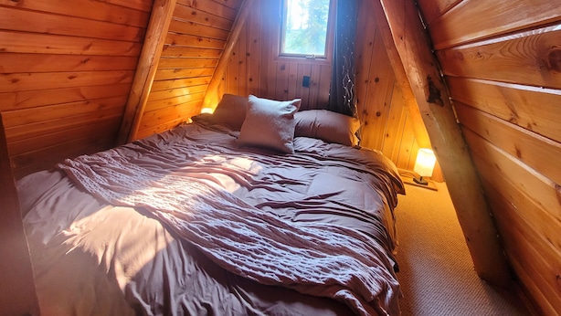 Une chambre confortable située dans les combles, avec un plafond en pente, des murs en bois, un lit avec des oreillers, une table de chevet et une fenêtre offrant une belle vue.
