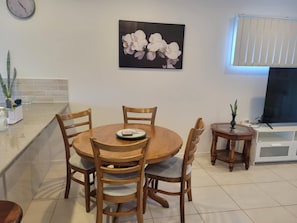 A dining area with a round wooden table and four chairs, a clock on the wall, and a potted plant on the counter. - Villa 1 - Glass House Mountains Retreat (Beerwah)