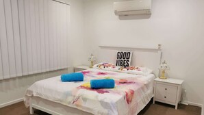 A bedroom with a bed, a nightstand, a lamp, a wall-mounted air conditioner, and a window with blinds. - Villa 1 - Glass House Mountains Retreat (Beerwah)