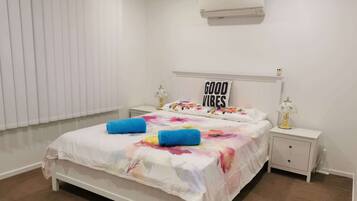 A bedroom with a bed, a nightstand, a lamp, a wall-mounted air conditioner, and a window with blinds.