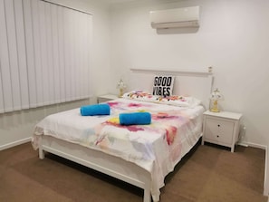 A bedroom with a bed, a nightstand, a lamp, a wall-mounted air conditioner, and a window with blinds. - Villa 1 - Glass House Mountains Retreat (Beerwah)