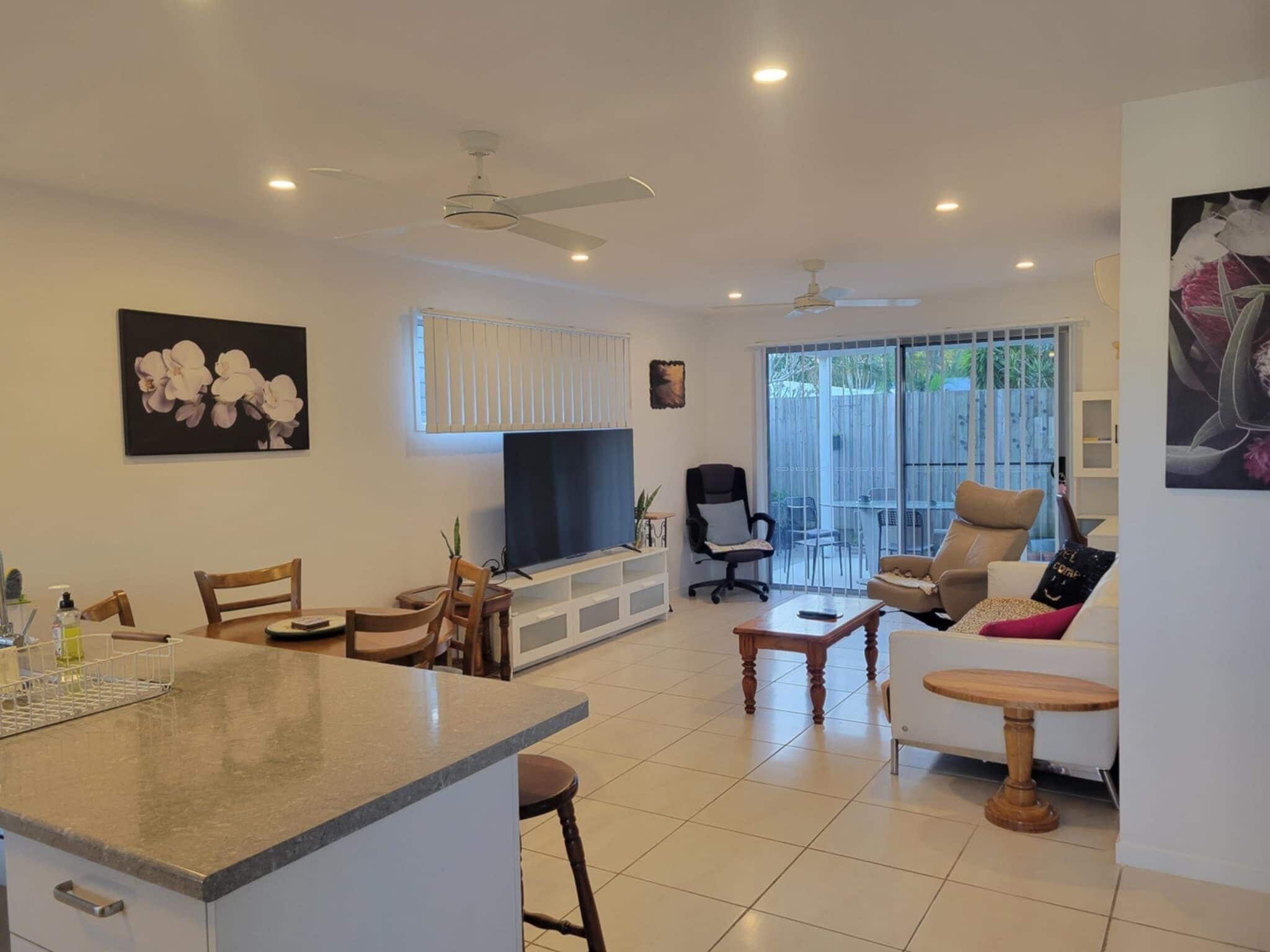 A spacious living area with a dining table, chairs, a sofa, a TV, and a balcony with sliding doors.