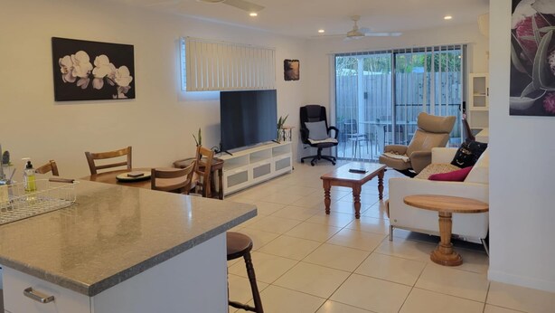 A spacious living area with a dining table, chairs, a sofa, a TV, and a balcony with sliding doors. - Villa 1 - Glass House Mountains Retreat (Beerwah)