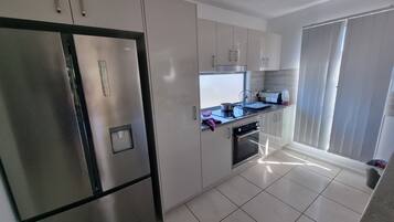A modern kitchen with stainless steel appliances, white cabinetry, and a tiled floor.