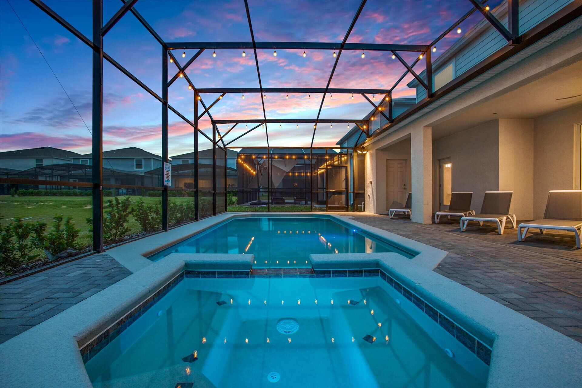 Une piscine entourée de parois en verre, avec des chaises longues et une vue sur les maisons au loin.