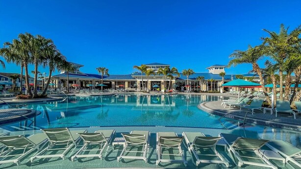 Ein Poolbereich eines Resorts mit klarem, blauem Wasser, Liegestühlen, Palmen und einem Gebäude mit blauem Dach.