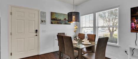 Un comedor con una mesa dispuesta para cuatro personas, una lámpara colgante y una ventana con persianas.