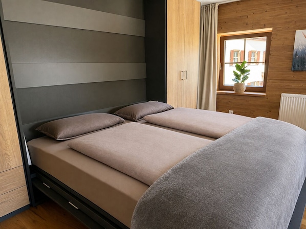 Un dormitorio moderno con cama, ventana con cortinas y radiador.