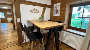 A dining area with a wooden table, black chairs, a potted plant, and a window with a view of greenery and buildings. - NEW! FRITZ-ALPCHALETS House Lechtal Apartment  "Stallkarspitze" right on the Lechweg (Vorderhornbach)