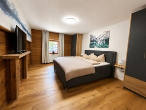 A bedroom with a bed, a television, a window with curtains, and a painting on the wall.