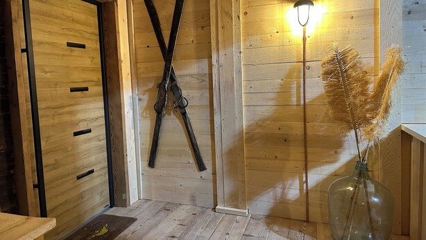 A wooden interior with a door, skis leaning against the wall, a lamp, and a vase with dried plants. - NEW! FRITZ-ALPCHALETS House Lechtal Apartment  "Stallkarspitze" right on the Lechweg (Vorderhornbach)