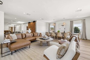 A modern living room with a sectional sofa, a round coffee table, and a dining area with a view. - The Big Yellow House Loft A (Summerland)
