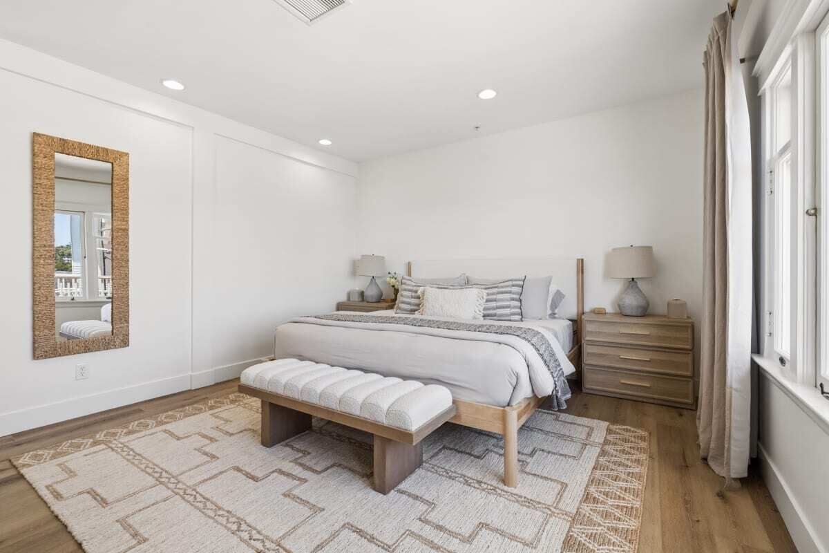Een slaapkamer met een bed, nachtkastjes, een bankje, een spiegel en een raam.