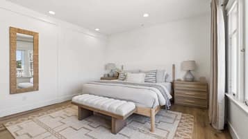 Een slaapkamer met een bed, nachtkastjes, een bankje, een spiegel en een raam.