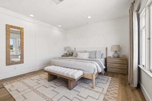 Een slaapkamer met een bed, nachtkastjes, een bankje, een spiegel en een raam.