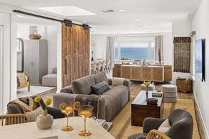 Een moderne woonkamer met een bank, salontafel en eethoek. Grote ramen bieden uitzicht op de oceaan.