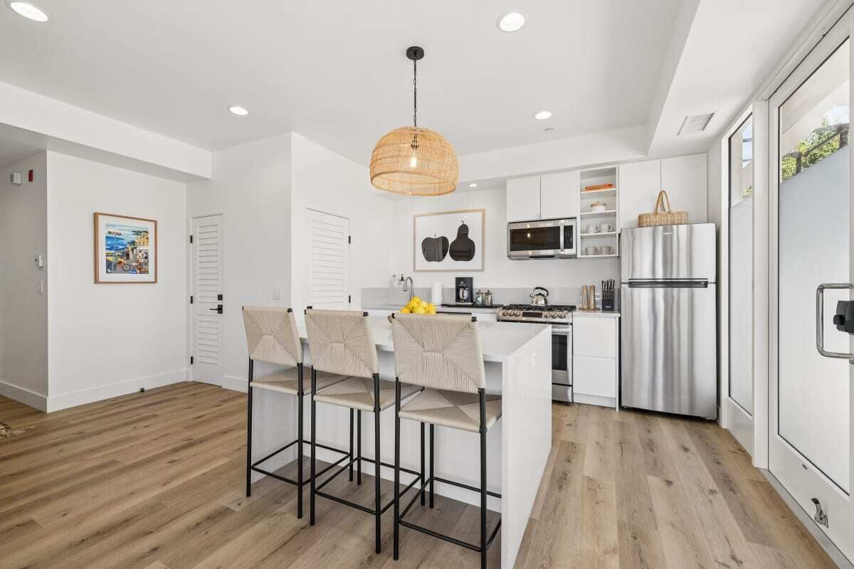 Una cocina moderna con armarios blancos, un refrigerador de acero inoxidable y una lámpara colgante.