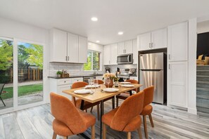 A modern kitchen with white cabinets, a stainless steel refrigerator, and a dining area with orange chairs. - Pipit Place - Pet-friendly Home w/ Fenced Yard (Fort Collins)