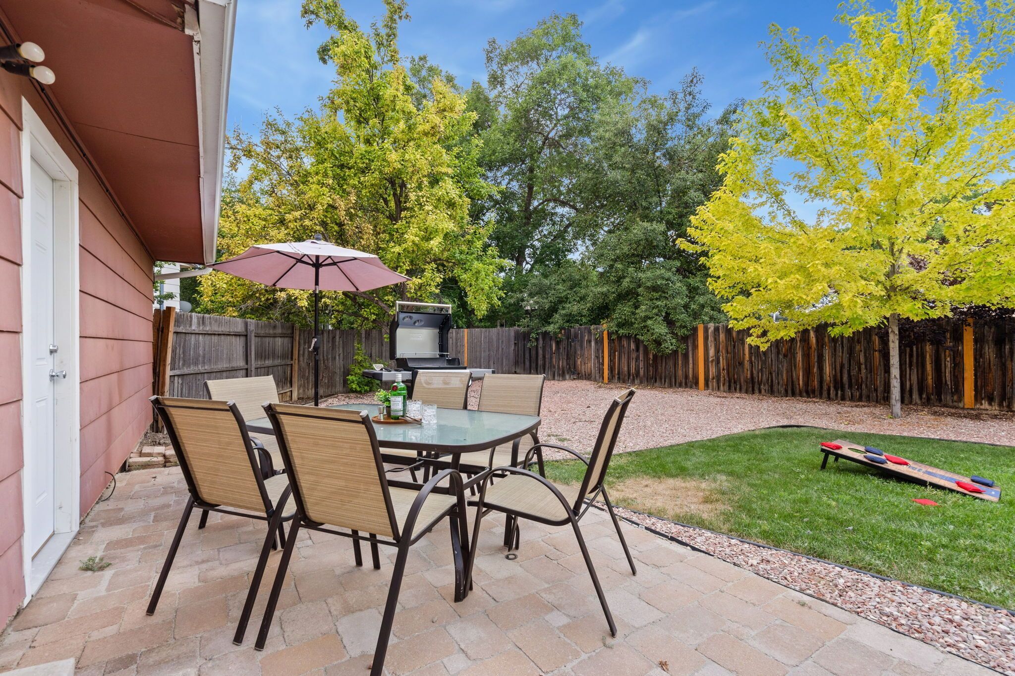 A patio with a table and chairs, a grill, and a wooden fence.