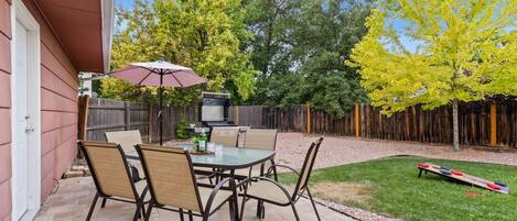 A patio with a table and chairs, a grill, and a wooden fence.
