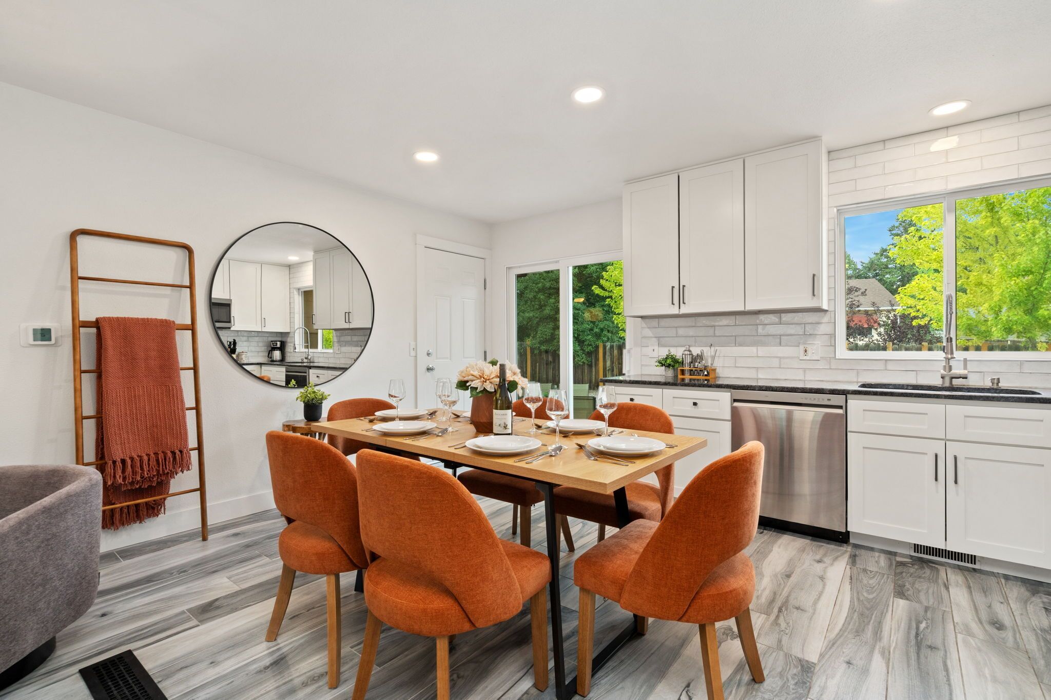 A modern kitchen with white cabinets, a dining table set for four, and a large window offering a view of greenery.