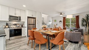 A modern kitchen with stainless steel appliances, a dining area with orange chairs, and a view of the outdoors through large windows. - Pipit Place - Pet-friendly Home w/ Fenced Yard (Fort Collins)