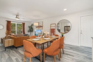 A modern living room with a sofa, a dining table set for four, and a large mirror.