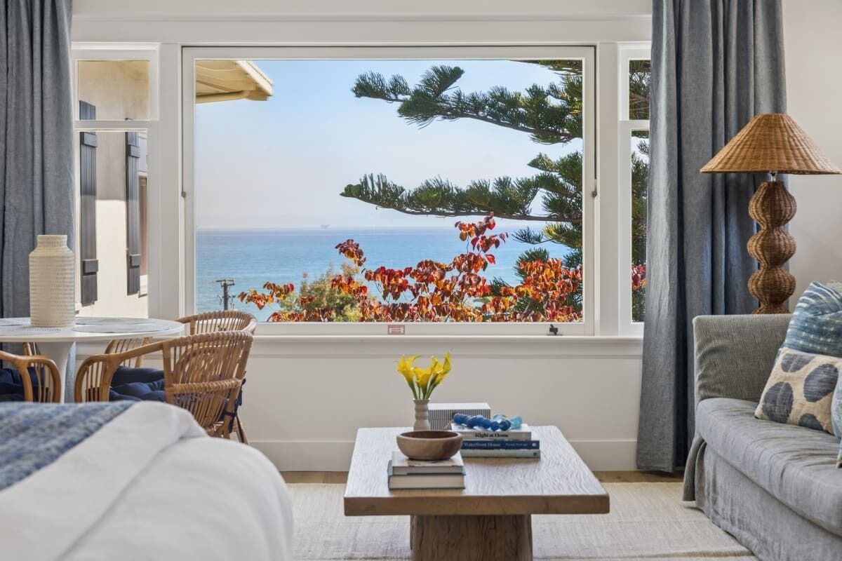 Una stanza con vista sul mare, un'area pranzo con sedie, un tavolo con libri e un vaso di fiori, e un divano con un cuscino decorato.