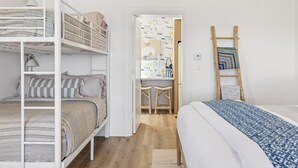 A bedroom with a bunk bed, a single bed, a desk with stools, and a ladder against the wall. - The Big Yellow House Loft B (Summerland)