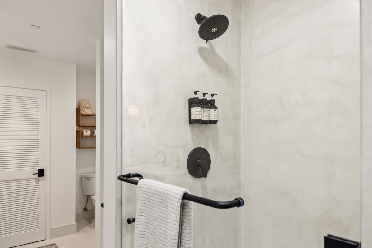 Un baño con ducha envuelta en vidrio, un perchero con toalla y un estante con artículos de aseo.
