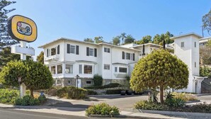 A two-story residential building with a white exterior, a driveway, and a well-maintained front yard with shrubs and a tree. - The Big Yellow House Loft B (Summerland)