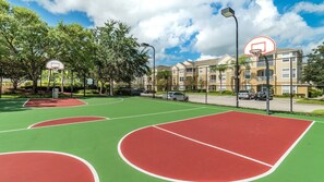 An outdoor basketball court with a green and red surface, surrounded by trees and a fence. - Last Minute Disney! Private Pool, Hot Tub, Game Room & Themed Bedrooms. Book Now! #113541 (Orlando)