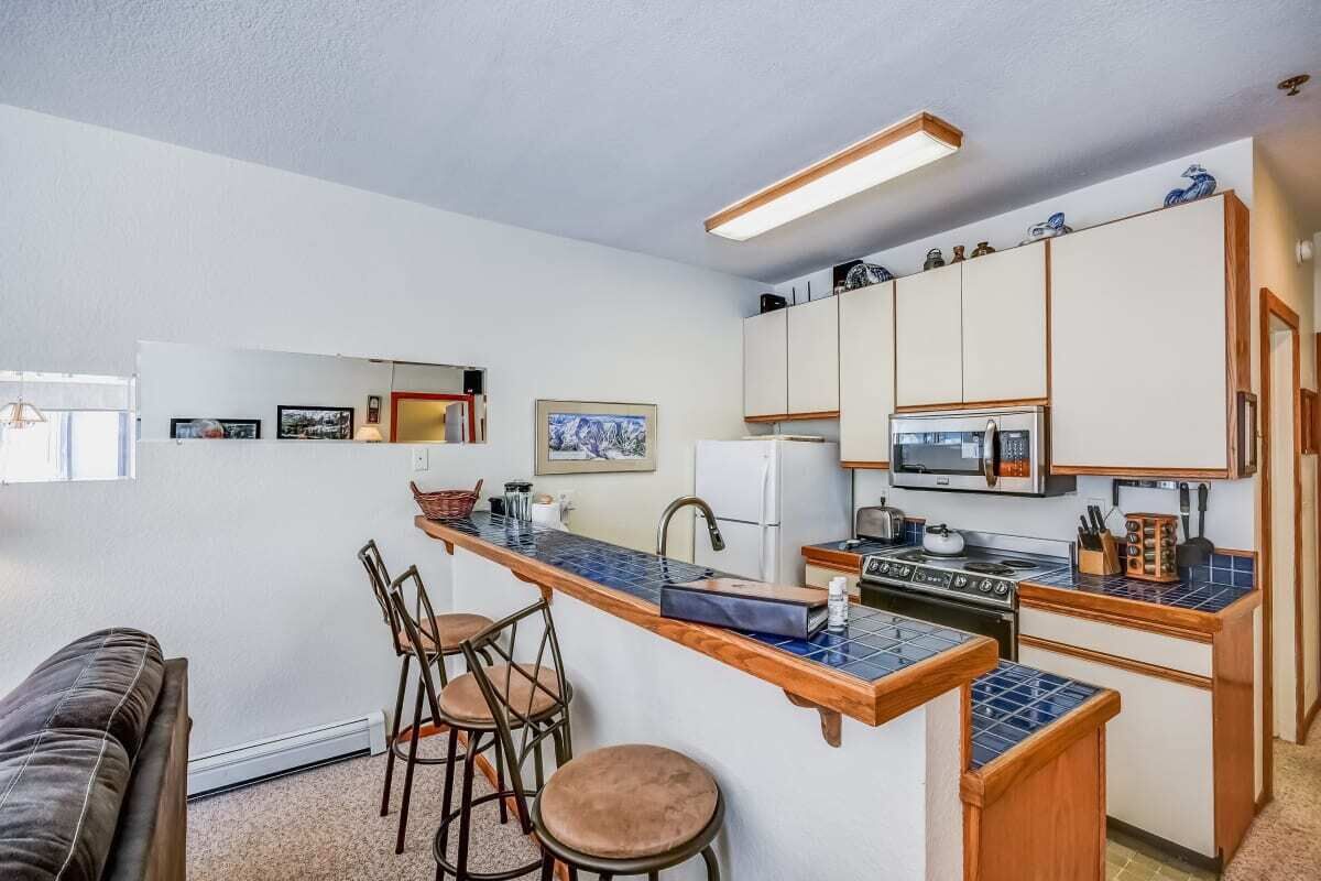 Cocina compacta con una isla central, taburetes de bar y un refrigerador.