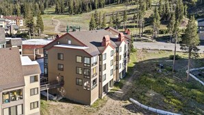 A multi-story building with a flat roof, surrounded by a natural landscape with trees and a hilly background. - Ski-In/Ski-Out Kirkwood Village Condo (Kirkwood)