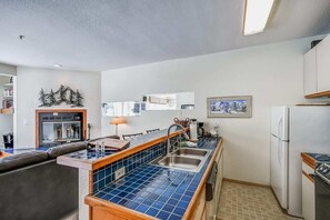A compact kitchen with a blue tiled backsplash, a built-in oven, and a refrigerator. - Ski-In/Ski-Out Kirkwood Village Condo (Kirkwood)