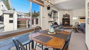 A dining area with a wooden table and chairs, a fireplace, and a view of neighboring buildings. - Ski-In/Ski-Out Kirkwood Village Condo (Kirkwood)