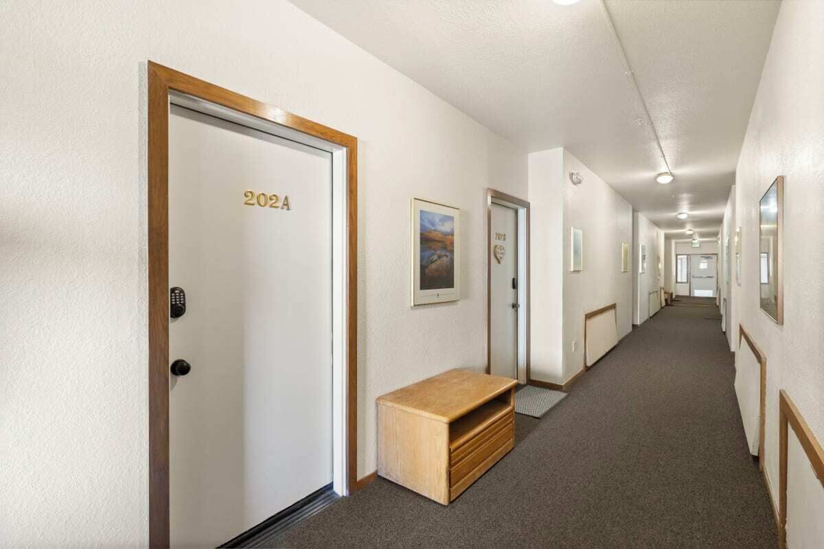 A hotel hallway with doors labeled with room numbers, a bench, and framed pictures on the walls.