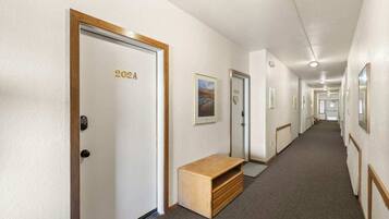 A hotel hallway with doors labeled with room numbers, a bench, and framed pictures on the walls.