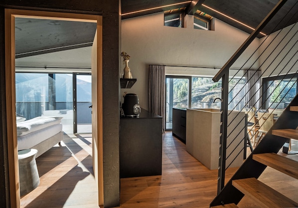 Un intérieur moderne avec un escalier en bois, un espace cuisine et une vue sur un paysage montagneux.