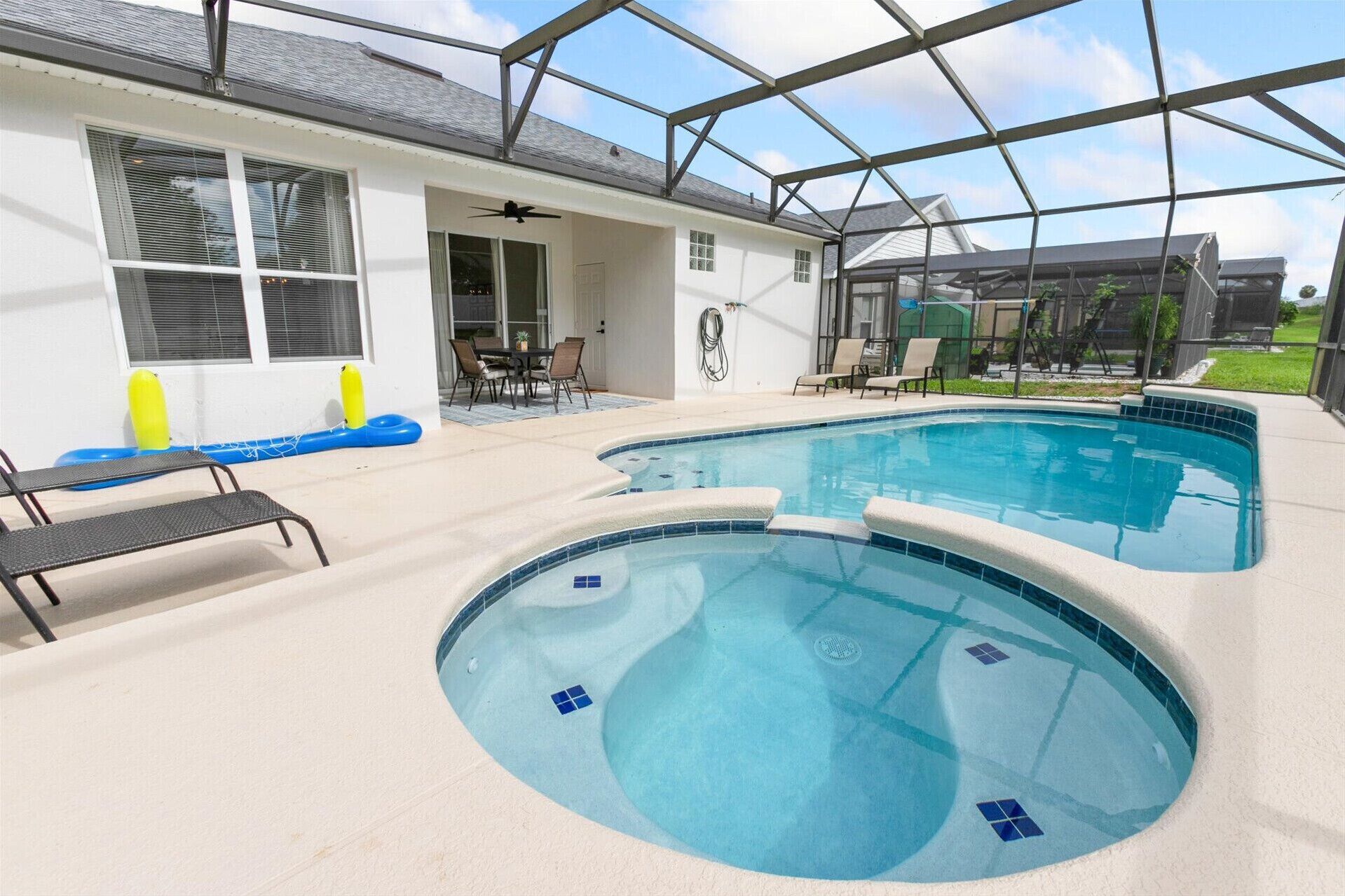 A swimming pool with a covered area, a patio with chairs, and a clear sky.