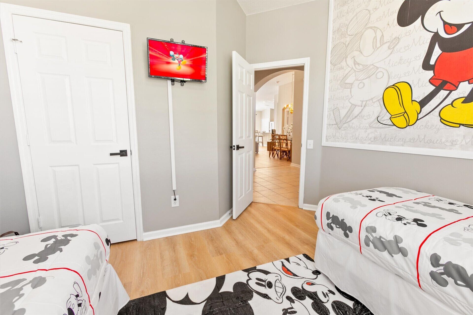 A hotel room with two beds, a television on the wall, and a Mickey Mouse mural.