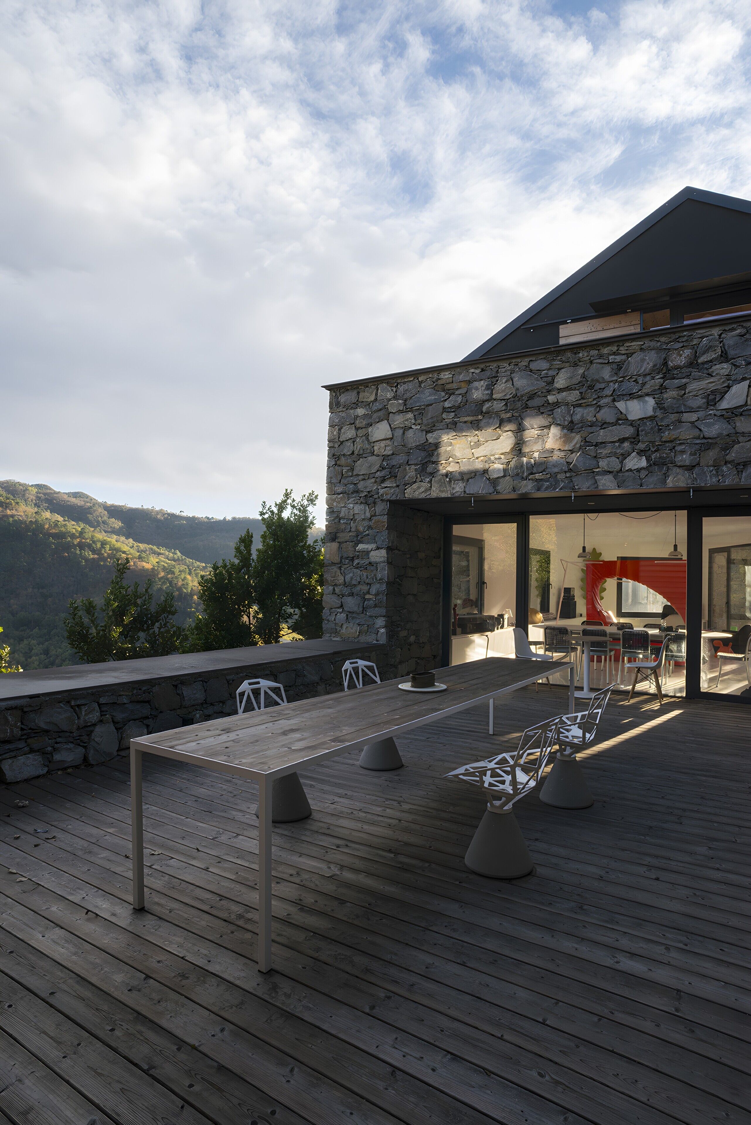 Un espace de restauration extérieur moderne, agrémenté d’un mur en pierre, d’une terrasse en bois et offrant une vue sur le paysage environnant.