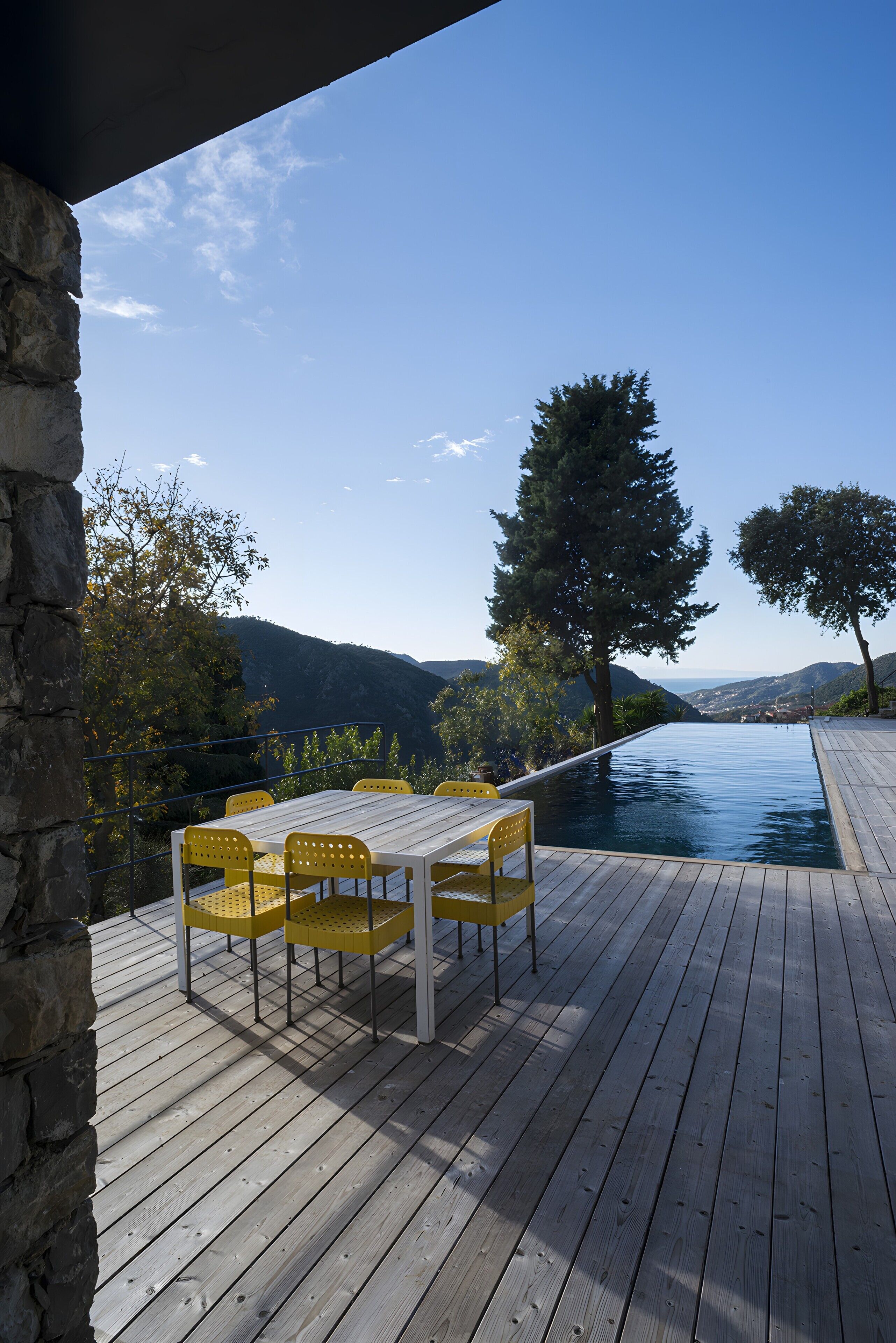 A wooden deck with a table and chairs, overlooking a pool and a mountainous landscape.